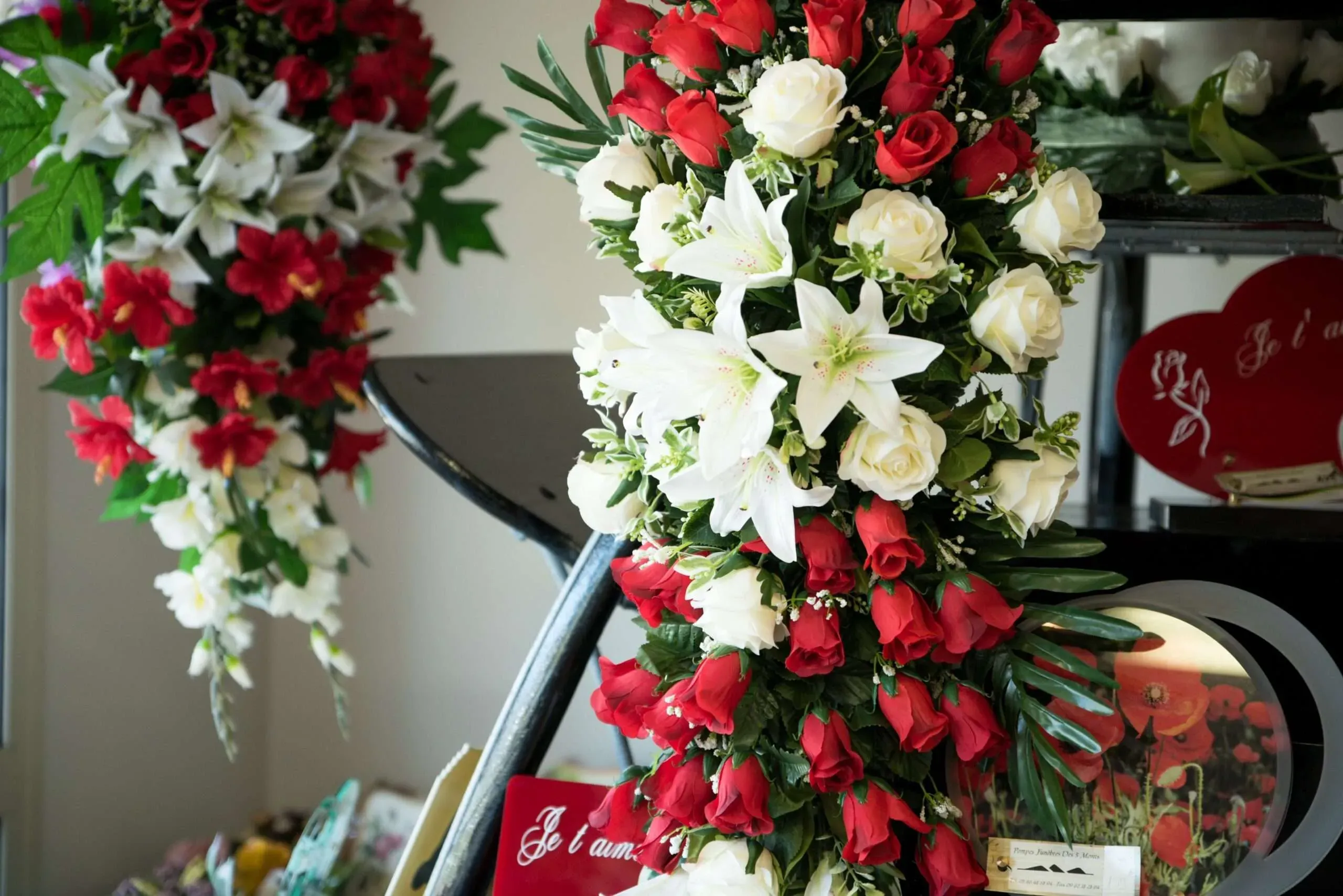 Composition florale de deuil en lierres, lys et roses rouges et blanches.