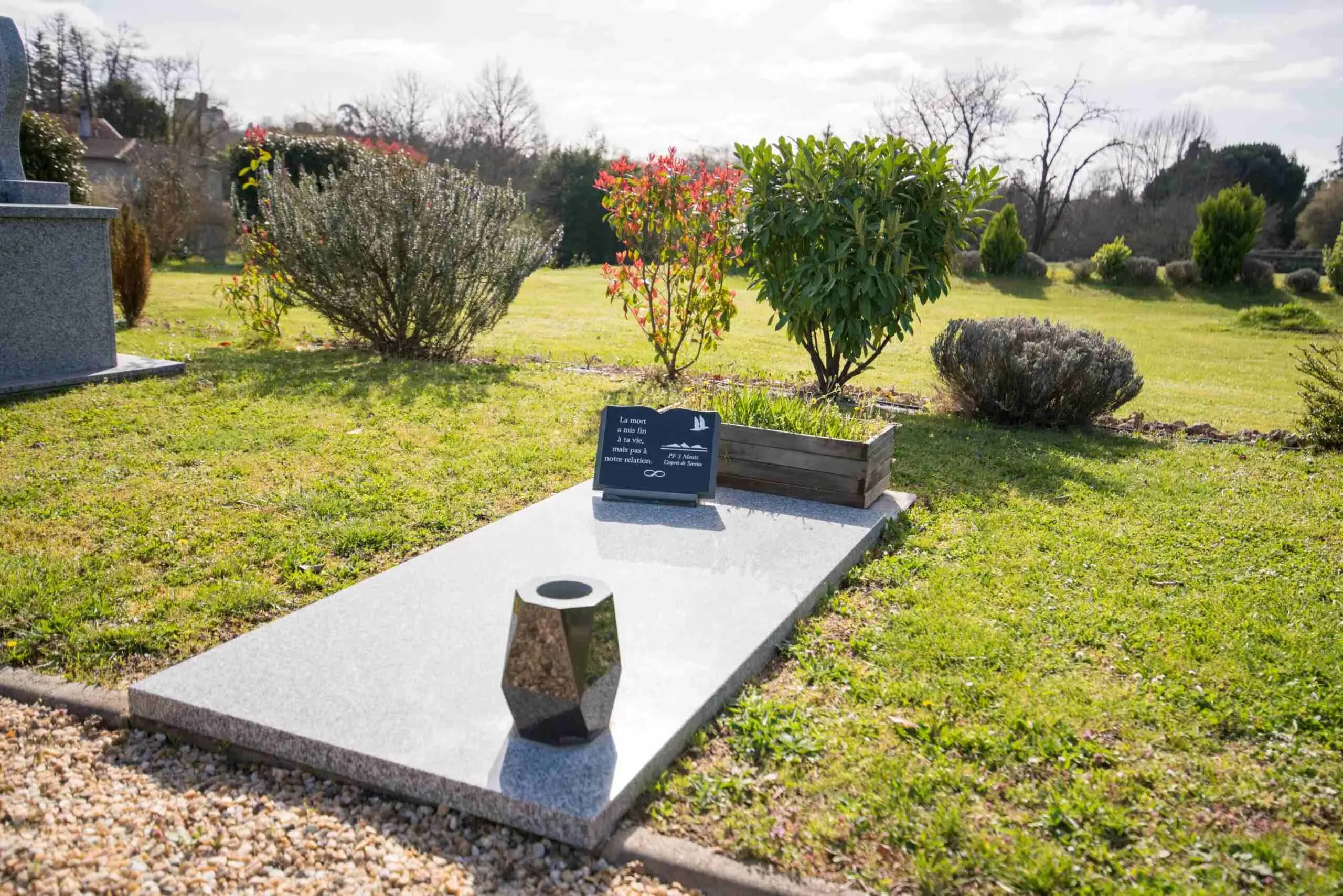 Plaque commémorative et urne posées sur une stèle funéraire dans un cimetière.