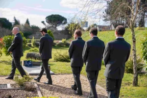Porteurs funéraires en costume sombre marchant dans un jardin du souvenir.